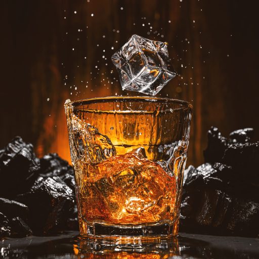 ice cubes fall into a glass with a brown alcoholic drink. splashes from falling ice fly in different directions