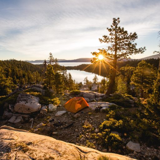 A beautiful shot of an orange tent on rocky mountain surrounded by trees during sunset